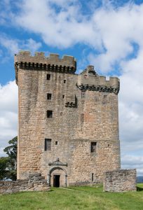 A medieval tower (Clackmannan Tower) sat set in green grassy surroundings, photographed against a blue sky with white, fluffy clouds.