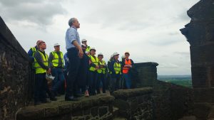 A group of people wearing hard hats and high vis looking out over the top of a stone building