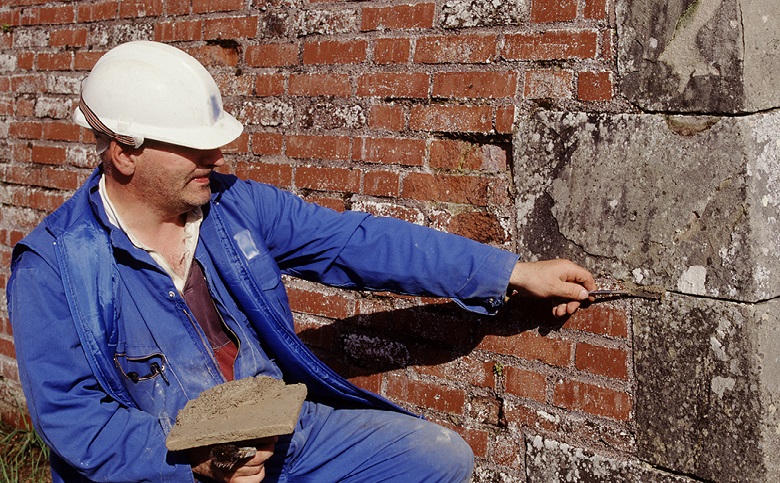 A person wearing a hard hat repointing mortar on a red wall
