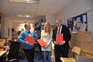 Three people holding up red folders in an office