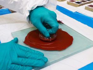 A person mixing red paint on a piece of glass