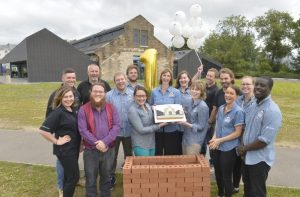 Staff stand outside the Engine Shed holding a big birthday cake and ballons