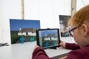 A child recording an animation using stick figurines and a photo of a traditional building