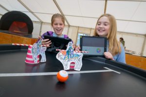 Two children use sphero robots and drawings of people jousting on a table