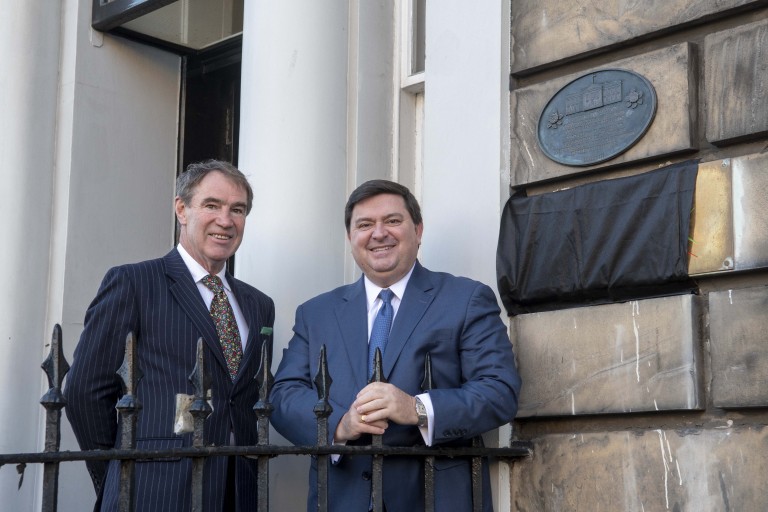 Two people stand smiling outside a new plaque on a traditional building