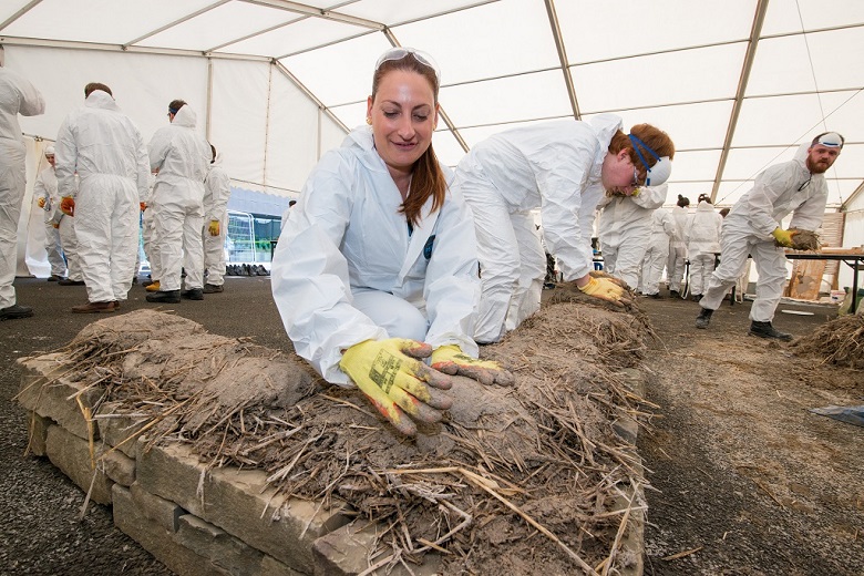 A person learning to build using mud and straw inside a gazebo