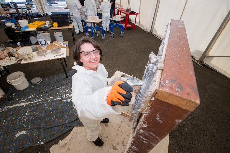 A person learning to lime mortar on a makeshift wall