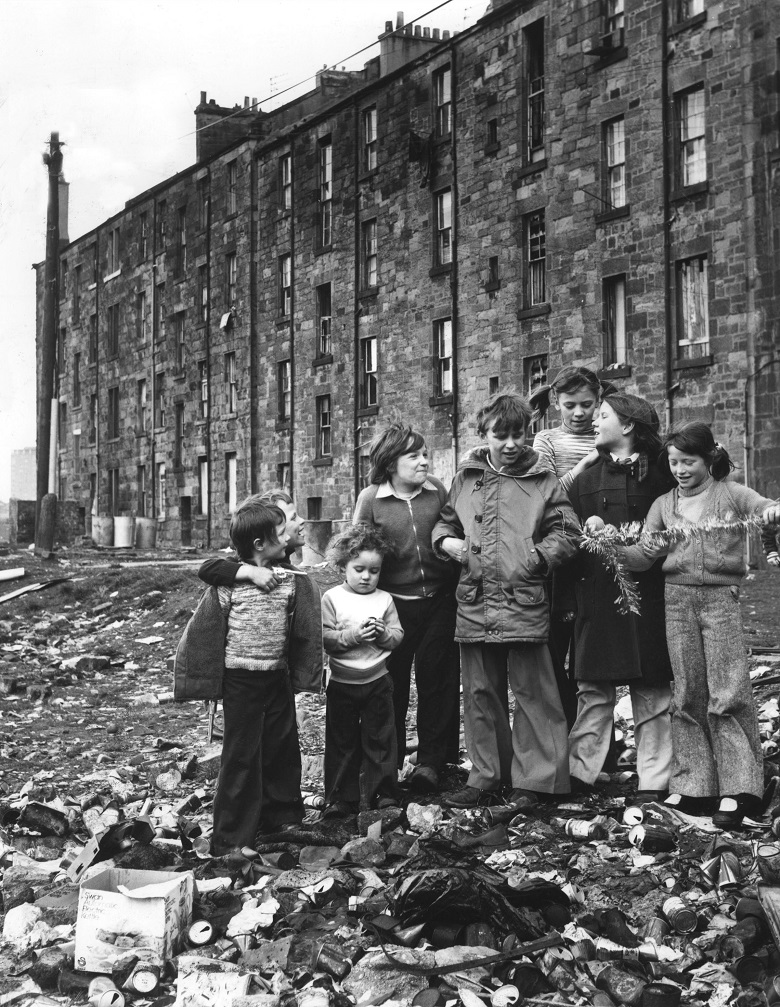 Children standing outside a block of tenement flats in a pile of rubbish