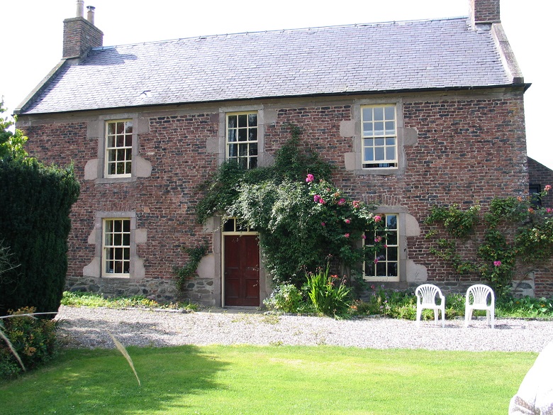 A large, brick house with six windows and two plastic chairs outside in the large garden