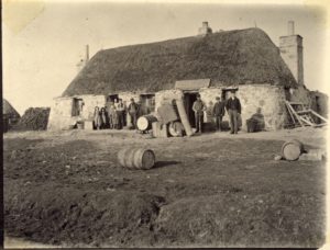 A group of people standing outside a standalone thatched building in the countryside