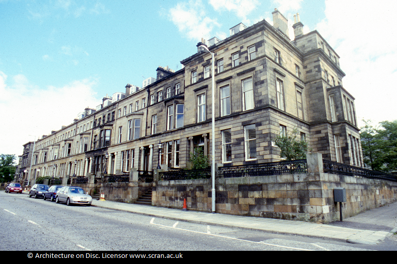 A block of stone buildings with a stone wall and iron railings outside