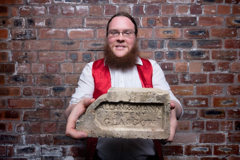 A person standing against a brick wall, holding a brick