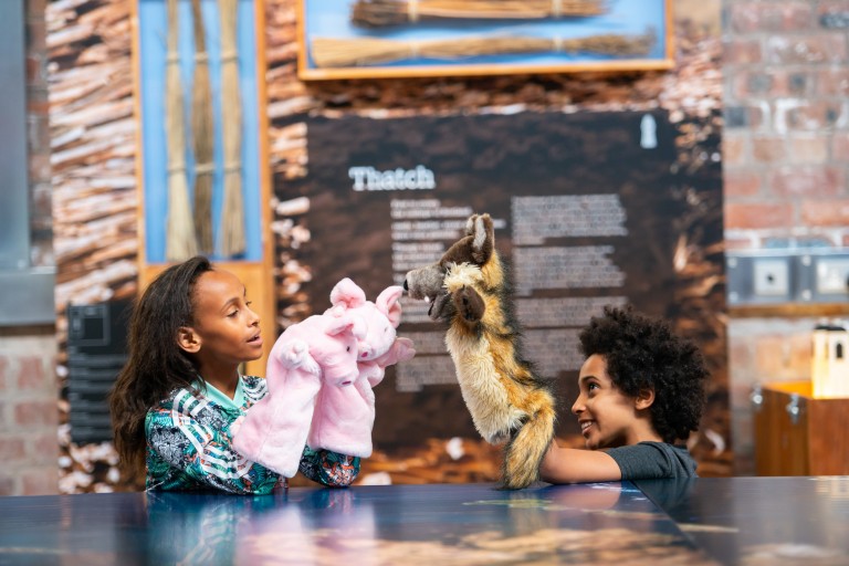 Two children play with wolf and pig puppets inside the Engine Shed.