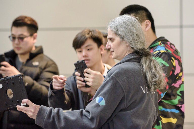 A person wearing a grey volunteer jumper, showing a group of visitors ipads.