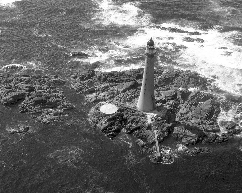 A tall lighthouse on a small area of rock
