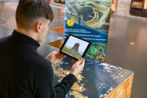 A person holding an ipad up to a giant floor map of Scotland