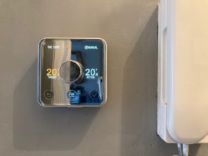 A smart, square digital thermostat mounted on a wall