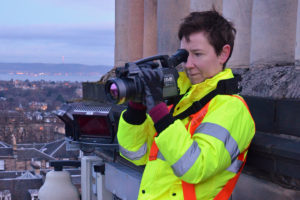 A person wearing high-vis vest, looking out through a large camera