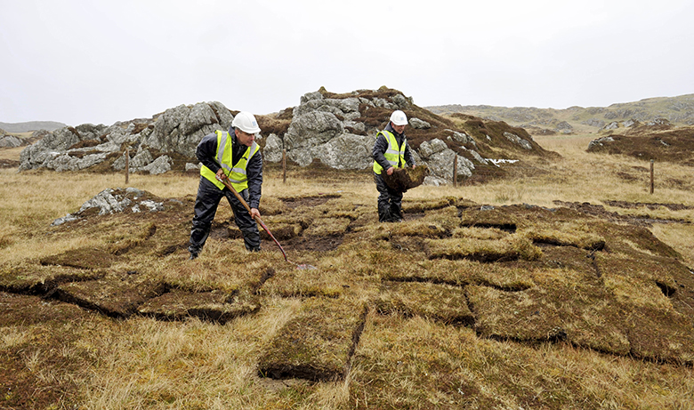 Two people working with squares of turf, earth building Scotland