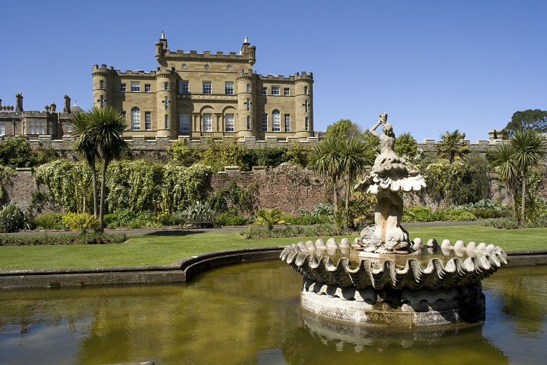 A stone fountain in front of a large, stone historic castle