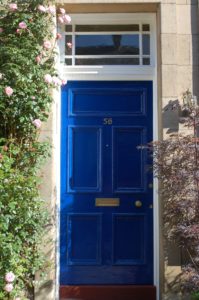 A blue, wooden front door with a small square window above the door