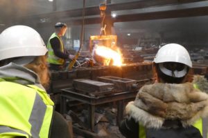 Two people watching someone work in an iron foundry