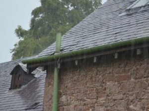 A stone house with a slate roof and iron drainpipe, in the pouring rain