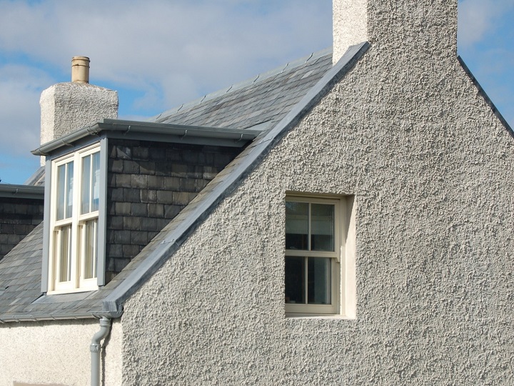 The gable end of a historic house with a slate roof and dormer windows