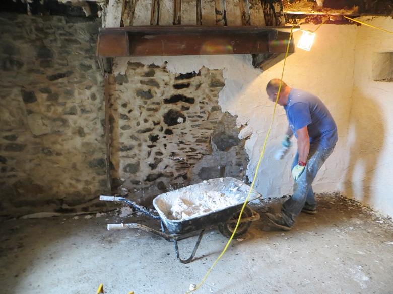 A person applying plaster from a wheelbarrow onto a stone interior wall