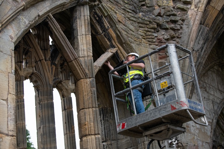 A person on a cherry-picker examining a historic stone abbey