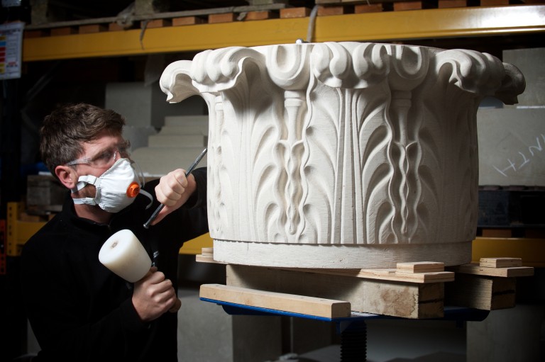 A person using a chisel to carve into a decorative building capital