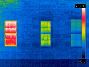 A thermal image showing a building with three windows. Red and green colours show heat being lost through the windows