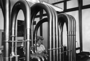 A woman working in an enclosed area, behind a series of tall, looped pipework