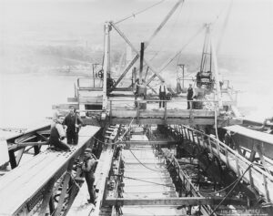 Four men, standing on steel beams forming part of the forth bridge, holding the tools to build it