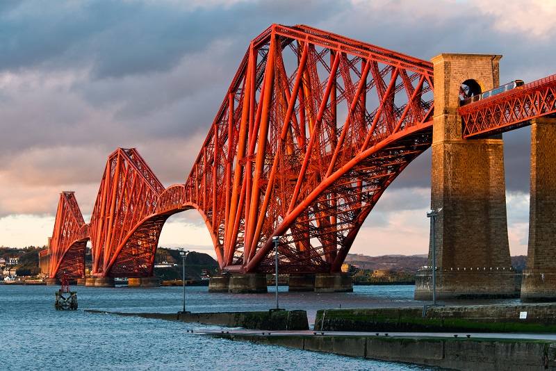 A large, complex, red rail steel bridge stretching across a huge estuary