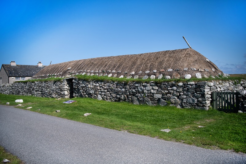 A long, narrow single-storey building made from stones stacked on top of each other. It has a thatched roof which is netted down with stones.