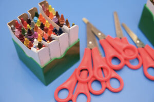 A box of different coloured crayons and a pile of small red-handled scissors