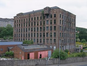 An industrial, six storey brick building, with at least 100 uniform, rectangular windows and a slate roof.