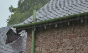 Rain pouring off a slated roof, with the gutter and drainpipe overflowing.