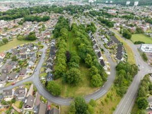 Aerial view of a straight section of trees with a central strip of grass. On either side are houses and roads with many parked cars.