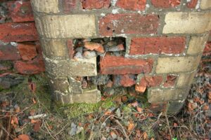 A section of curving brick wall next to the ground with many of the bricks crumbling, and some completely decayed away.