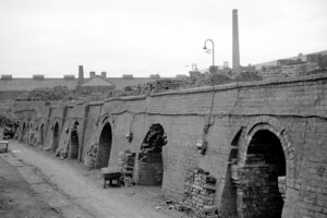 A black and white photo of a series of low arched brick tunnels. Many have stacked piles of bricks in their entrance or on the roof.