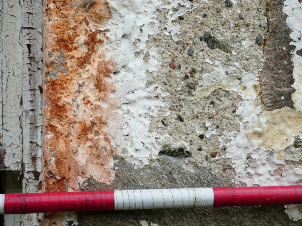 The weathered exterior of a historic building seen in closeup. An old limewash finish has weathered away leaving the masonry many different colours and flaking away. There is a red and white surveyor's pole for scale.