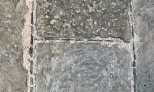 The weathered exterior of a historic building seen in closeup. The mortared stones are divided by limewash giving a square grid shaped pattern. Small pieces of dark slate have been pushed into the joints.