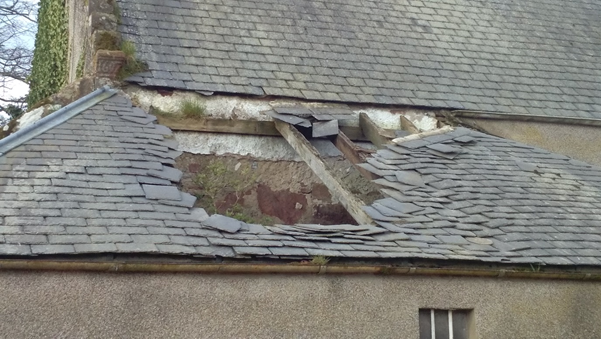 The collapsed tile roof of a building reveals a wall covered in limewash. The tiles have fallen into the centre with many overhanging the ten foot wide hole.