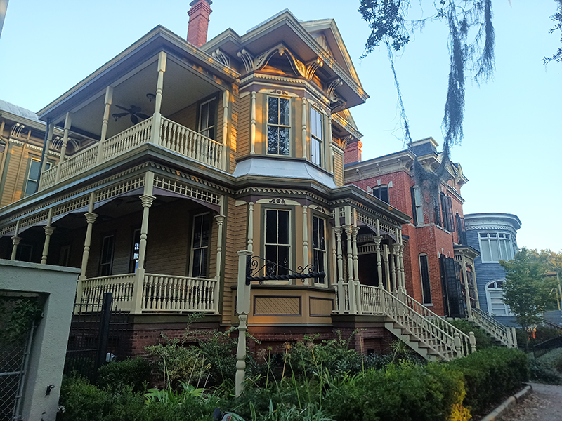 A row of green, pink and blue, large, detatched houses with bay windows and wooden baloncies