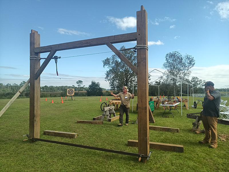 Two people raising up a wooden, square frame in a grassy area