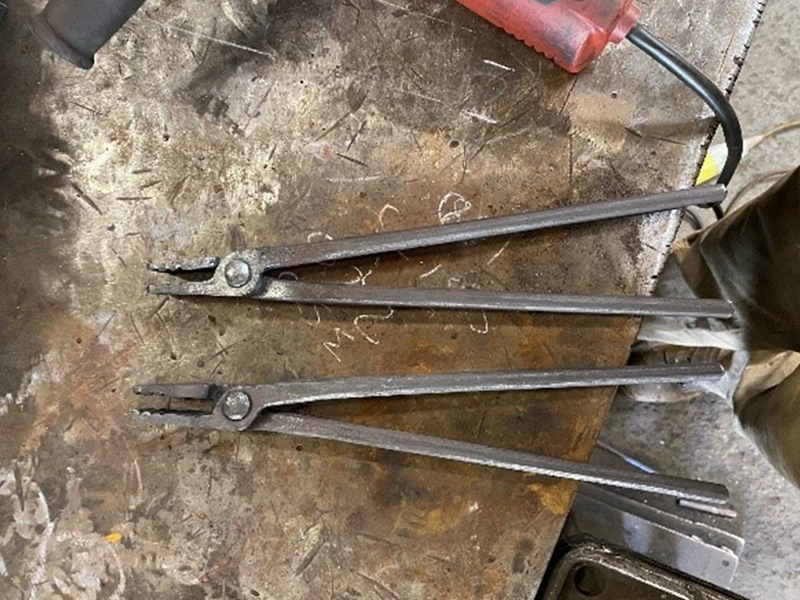 Two large pairs of metal tongs on a workshop table, with long handles.