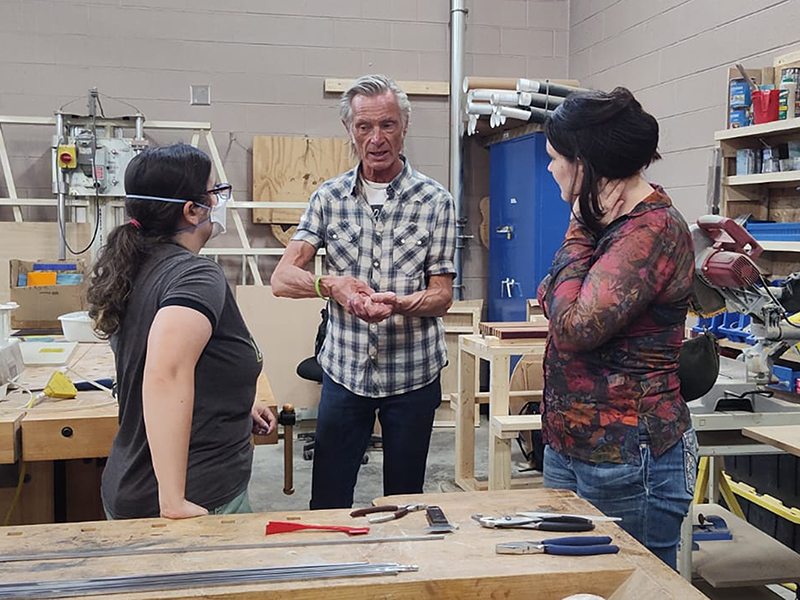 A person giving a talk to two people in a craft skills workshop