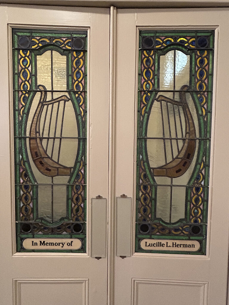 Two stained glass windows incorporated into a set of double doors. They feature a blue, green and yellow celtic design border, and two harps in the middle